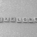 Monochrome Scrabble tiles spelling 'EXPLORE' on a glitter background.