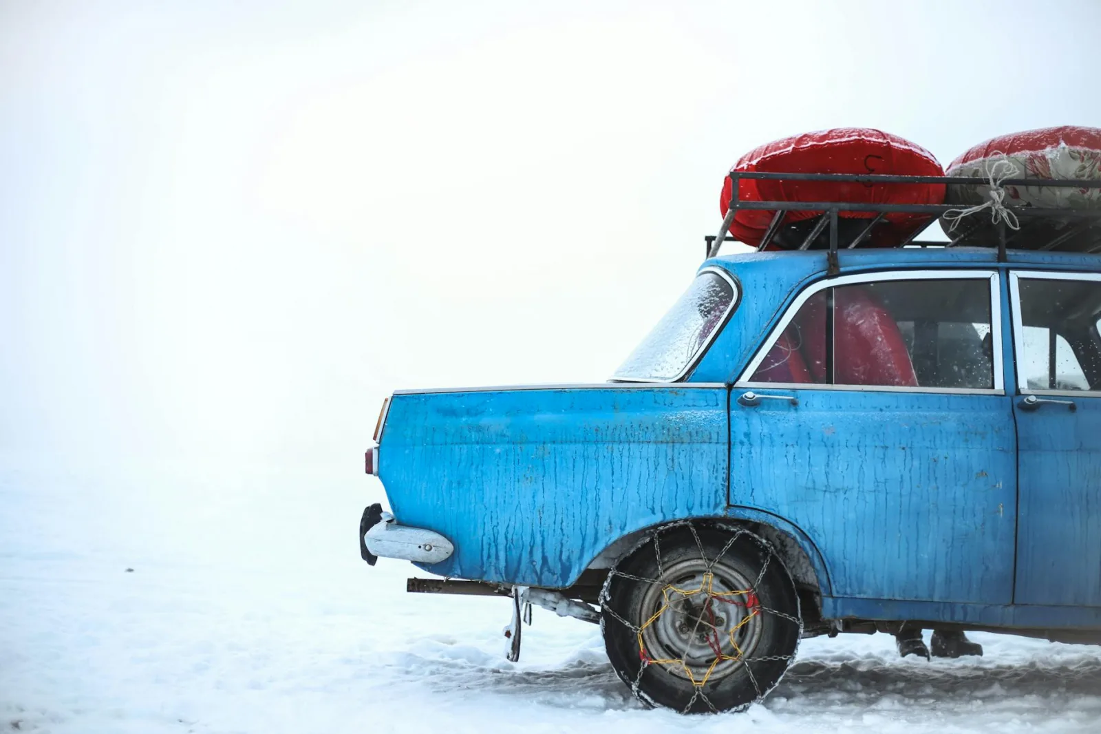 A vintage blue car with roof luggage in snowy Ak-Talaa, Kyrgyzstan.