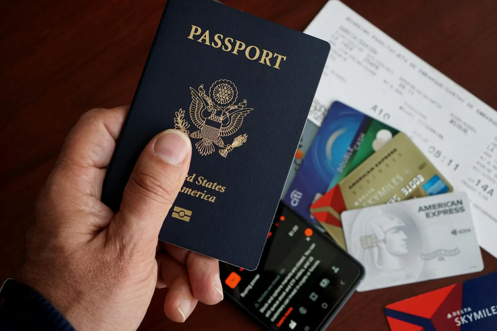 A close-up of a US passport with credit cards, tickets, and a mobile phone on a table.