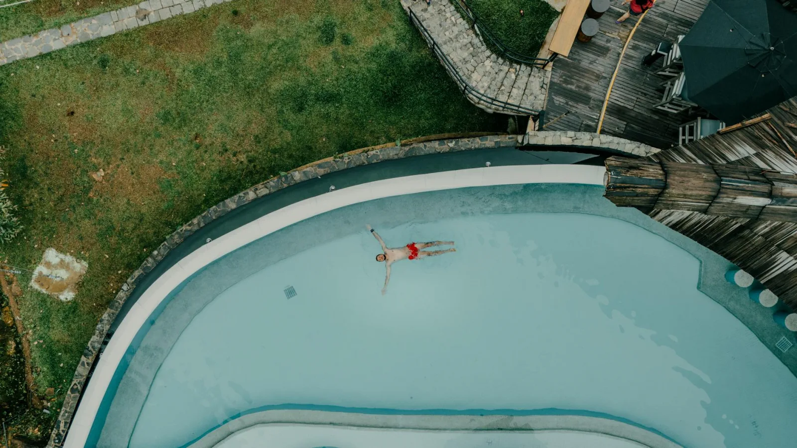 Aerial shot of a man floating peacefully in a resort pool surrounded by lush greenery, Sri Lanka.