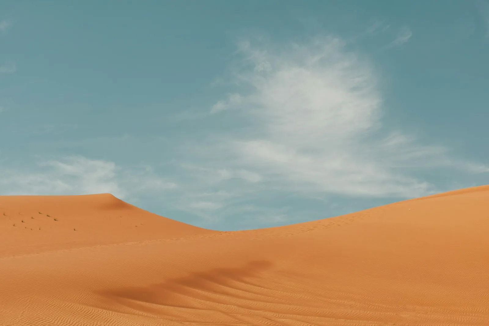 Serene view of wave-like sand dunes under a blue sky in Dubai's Arabian desert.