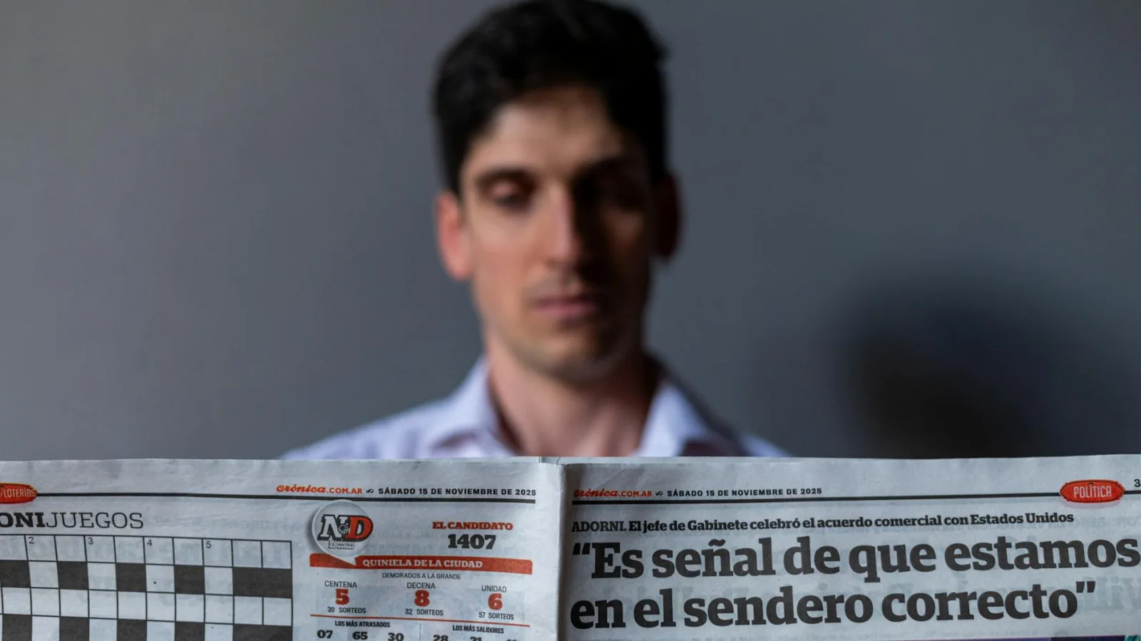Man holding a Spanish newspaper with headline and date visible, indoors.