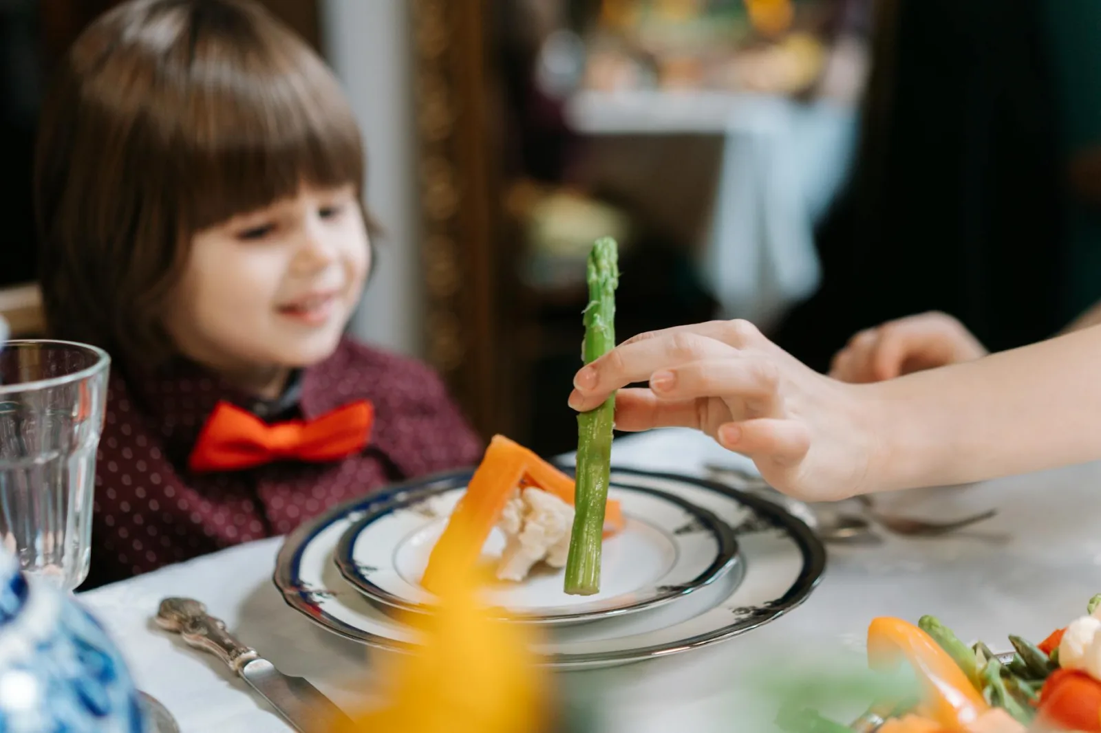 A child with a bow tie sits at a table enjoying a fine dining experience with healthy foods.