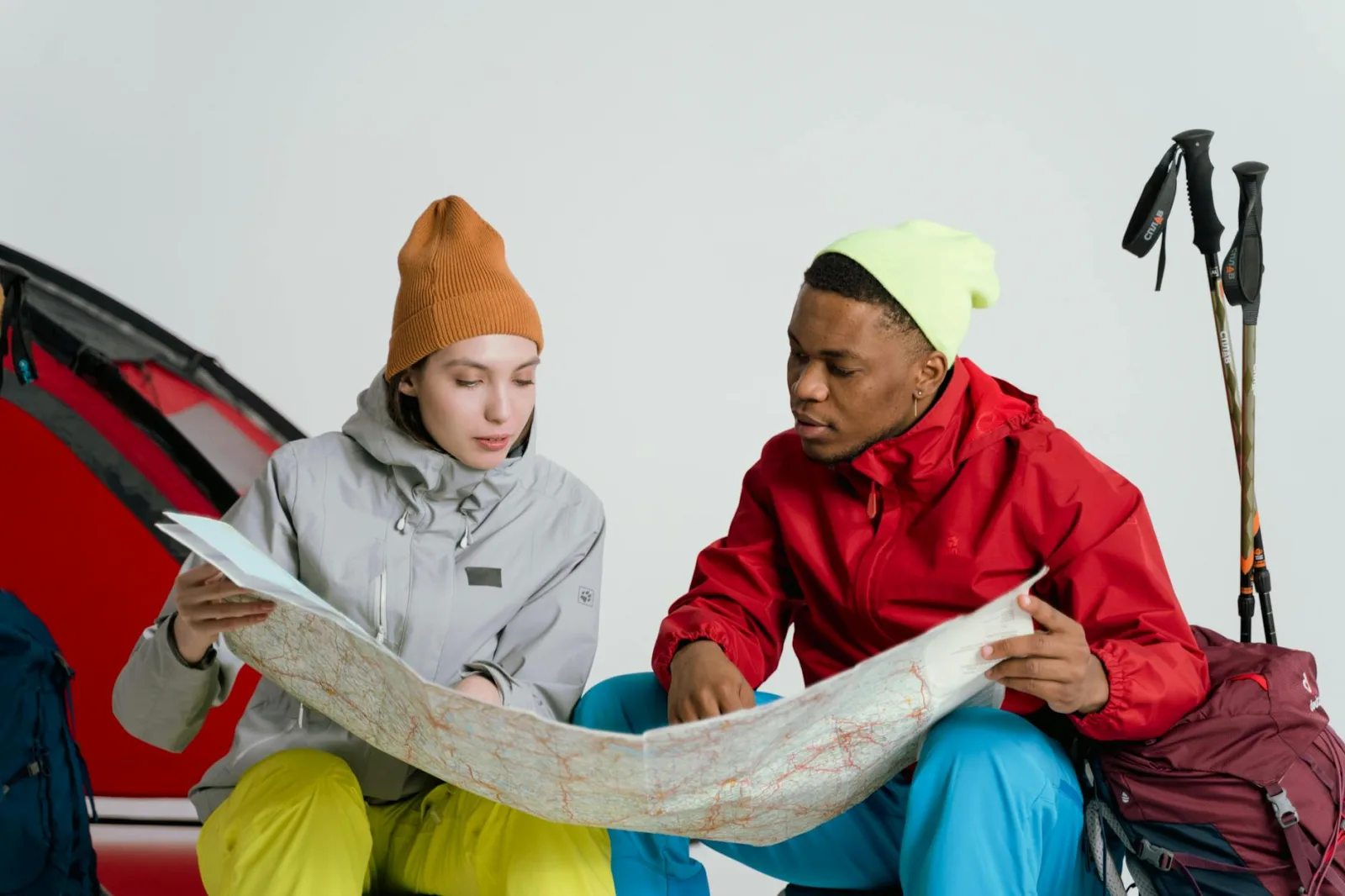 Two adventurers in vibrant winter gear planning a trip with a map indoors.