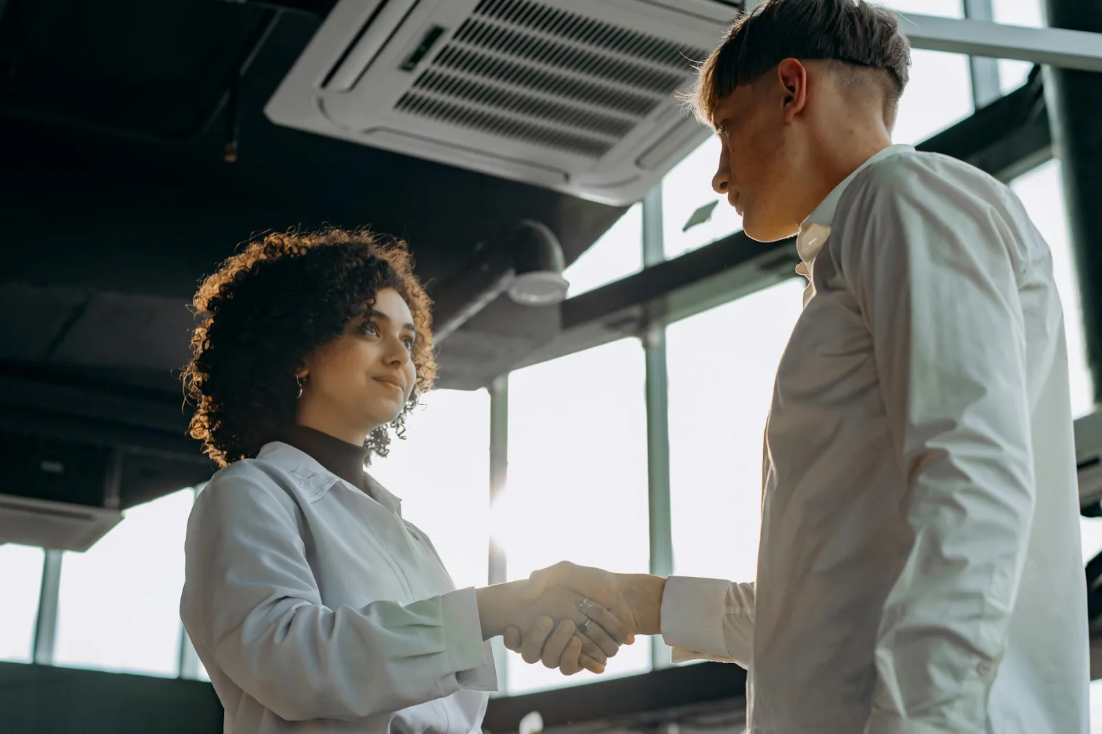 Business professionals exchange a handshake in a modern office setting, symbolizing collaboration.