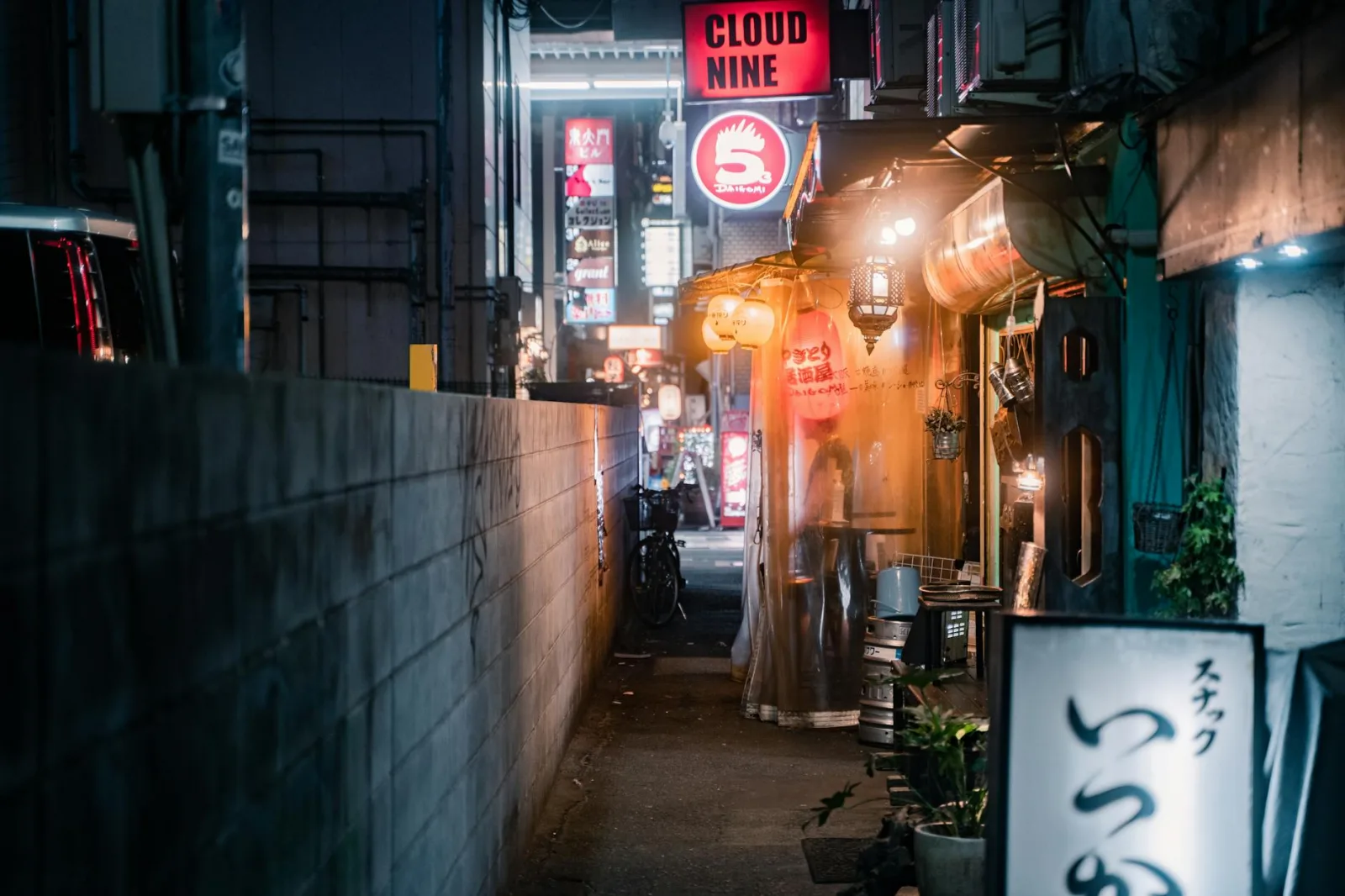 Explore the lively atmosphere of a narrow alleyway in Osaka at night, illuminated by bright neon signs.