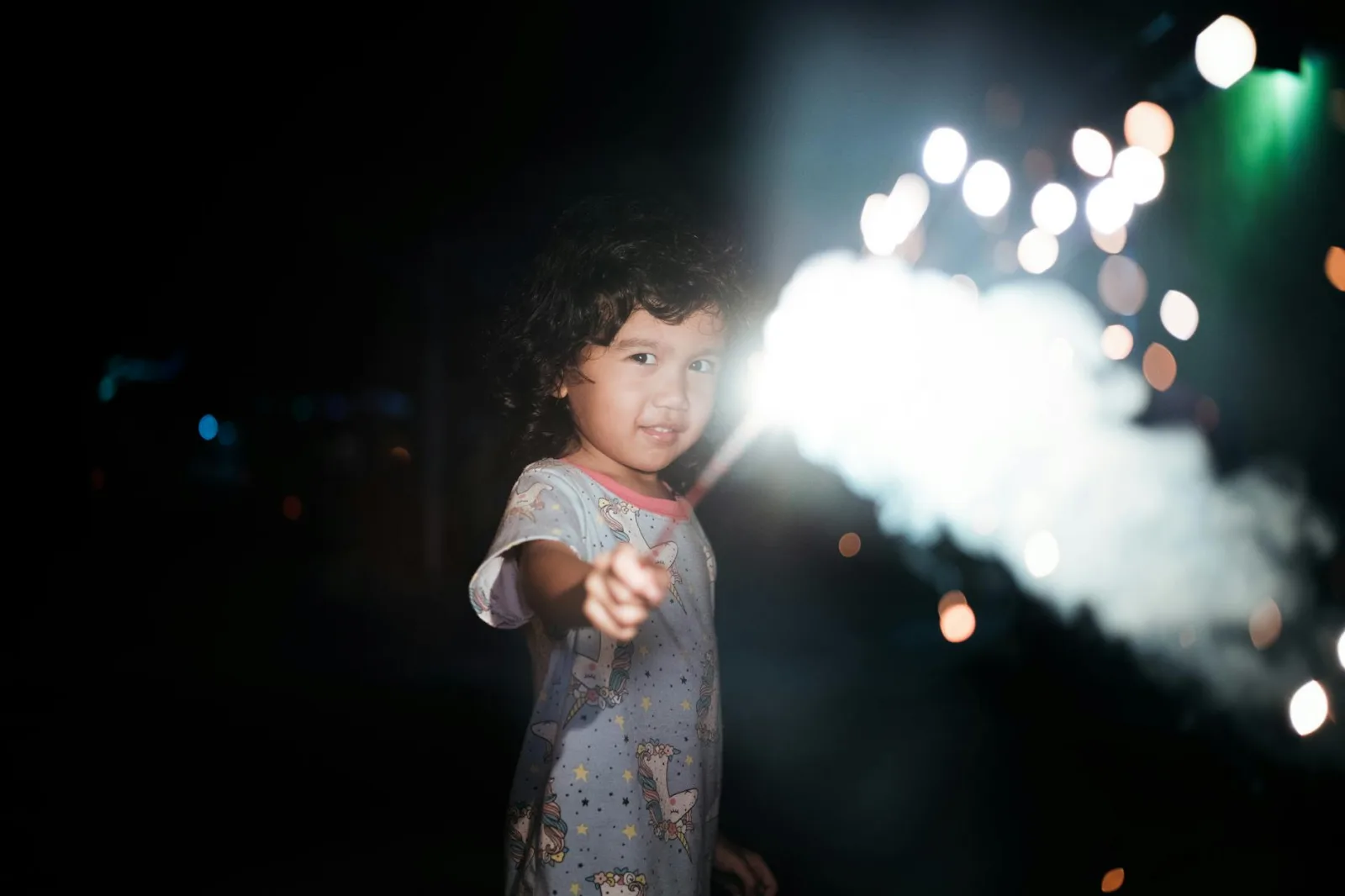 A young girl with a sparkler in hand lights up the night with joy and wonder.