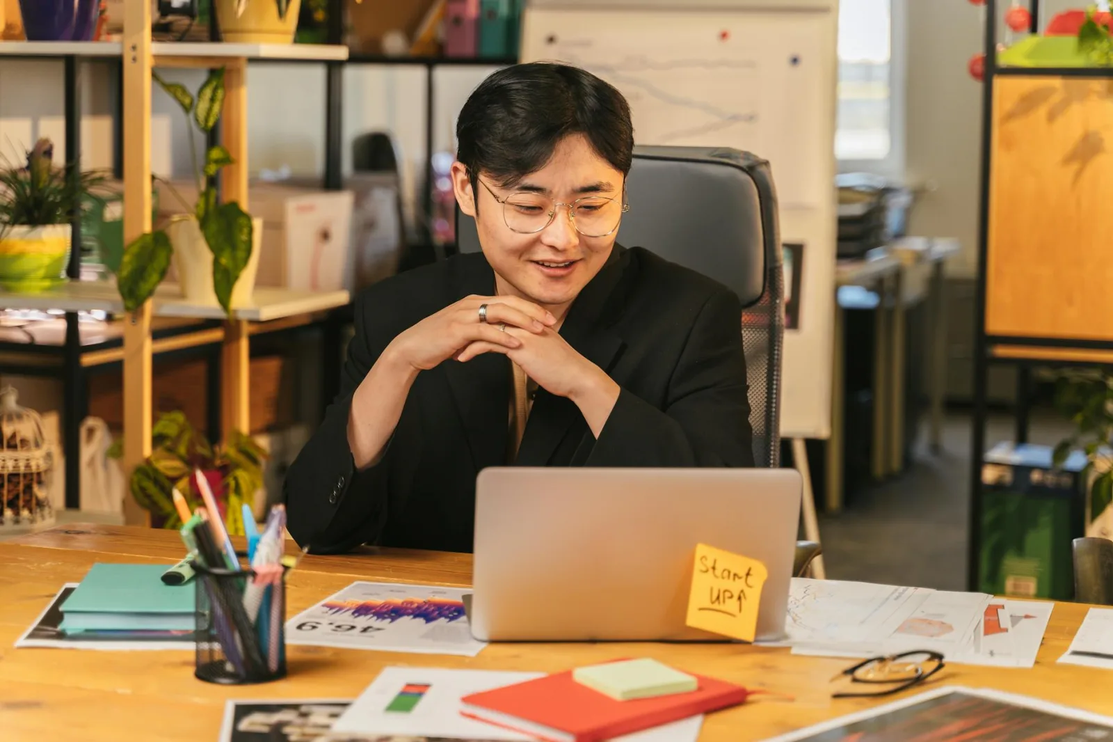 Asian man working happily in a modern office with a laptop, representing startup culture.