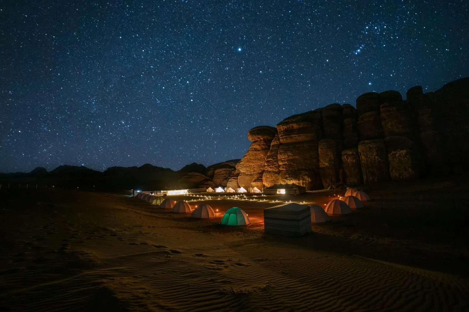 Breathtaking view of a starry night sky over a desert campsite in Tabuk, Saudi Arabia, with dramatic rock formations.