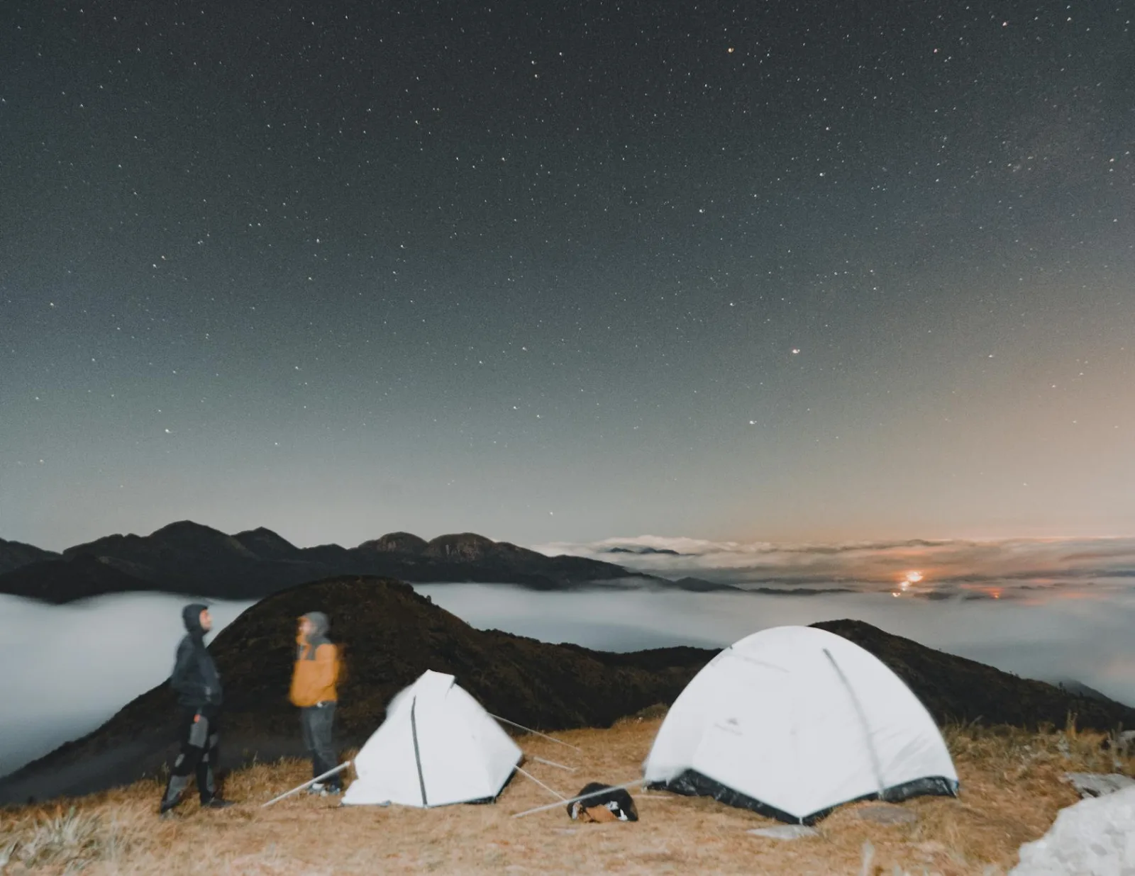 A breathtaking campsite with tents under a star-filled sky and mountain silhouettes.