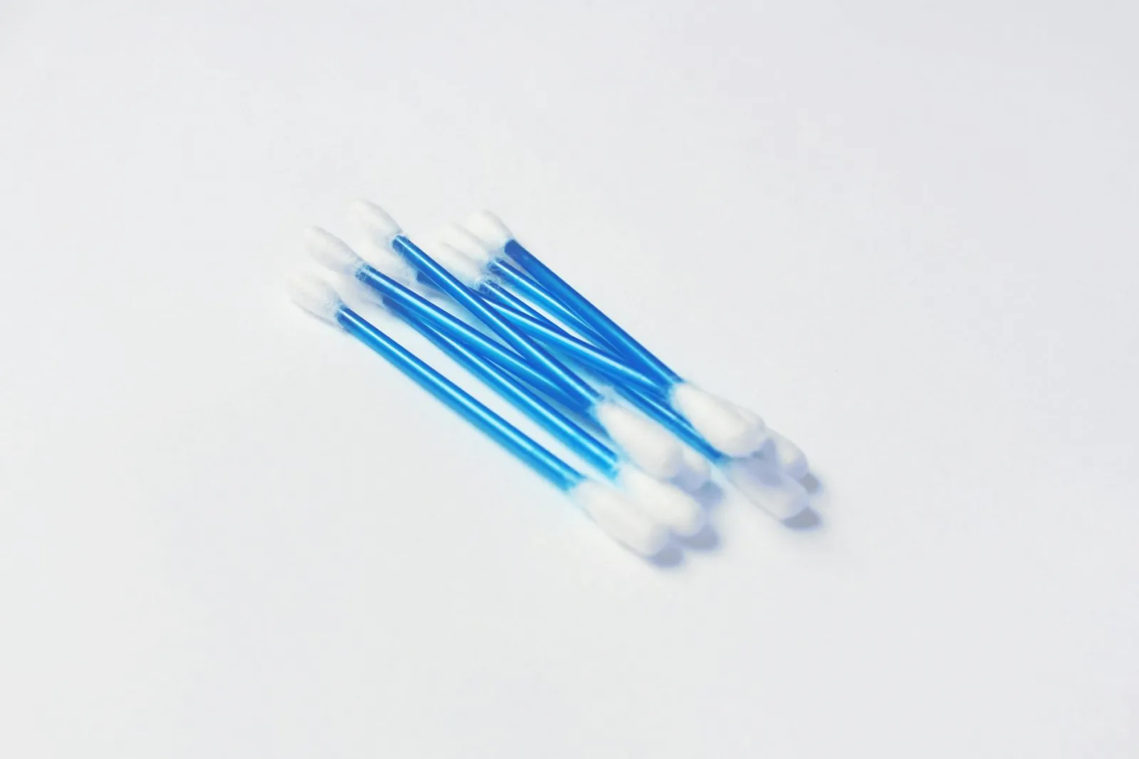 A minimalistic close-up image of blue handled cotton swabs on a white surface.
