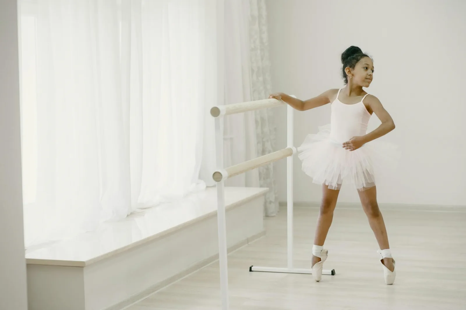 A young ballerina in a tutu practicing ballet at an indoor studio with natural light.