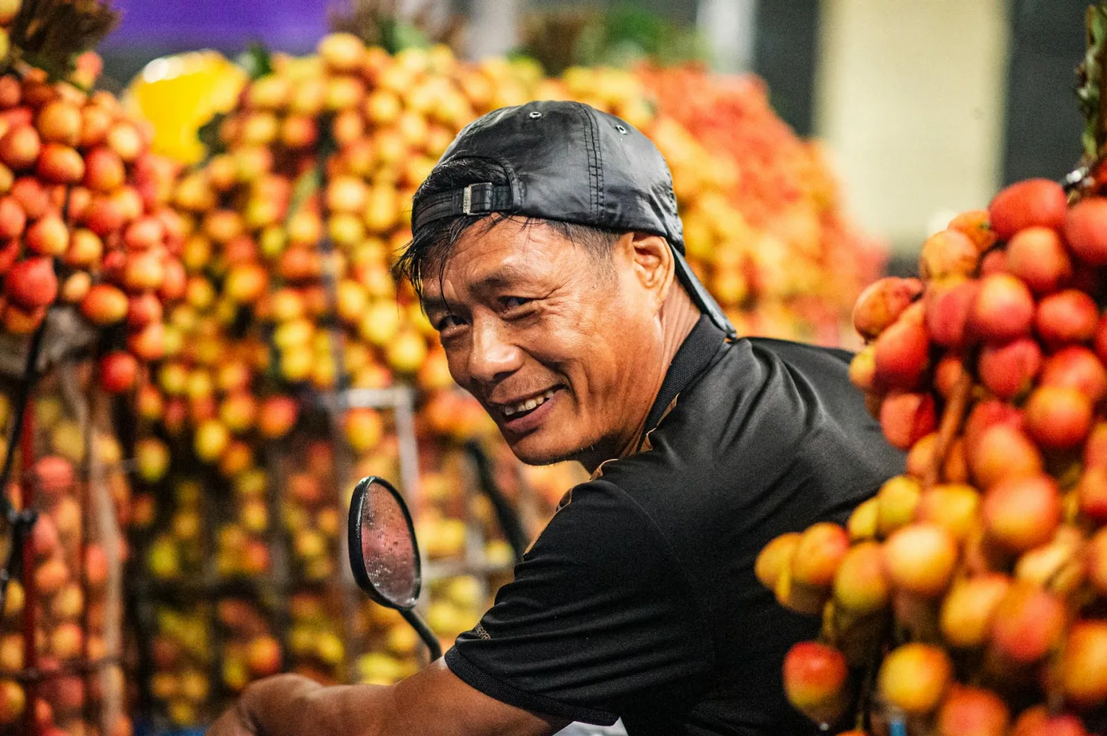 A joyful vendor at a lychee market in Bac Giang, Vietnam, surrounded by fresh fruit.