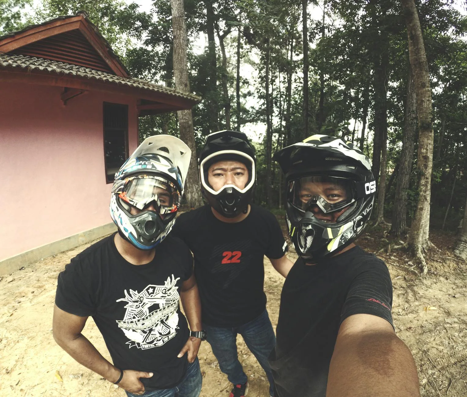 Three friends in helmets taking a selfie during a dirt biking adventure in a forest setting.