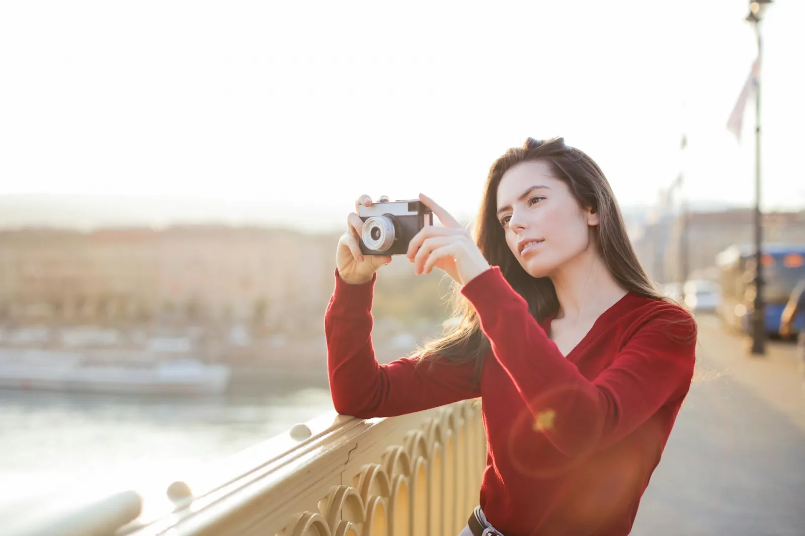 A woman in a red sweater takes a photo on a bridge during sunset, showcasing photography passion.