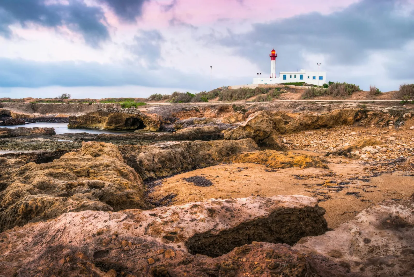 Stunning coastal view of Mahdia Lighthouse with rocky shore under a colorful sky.