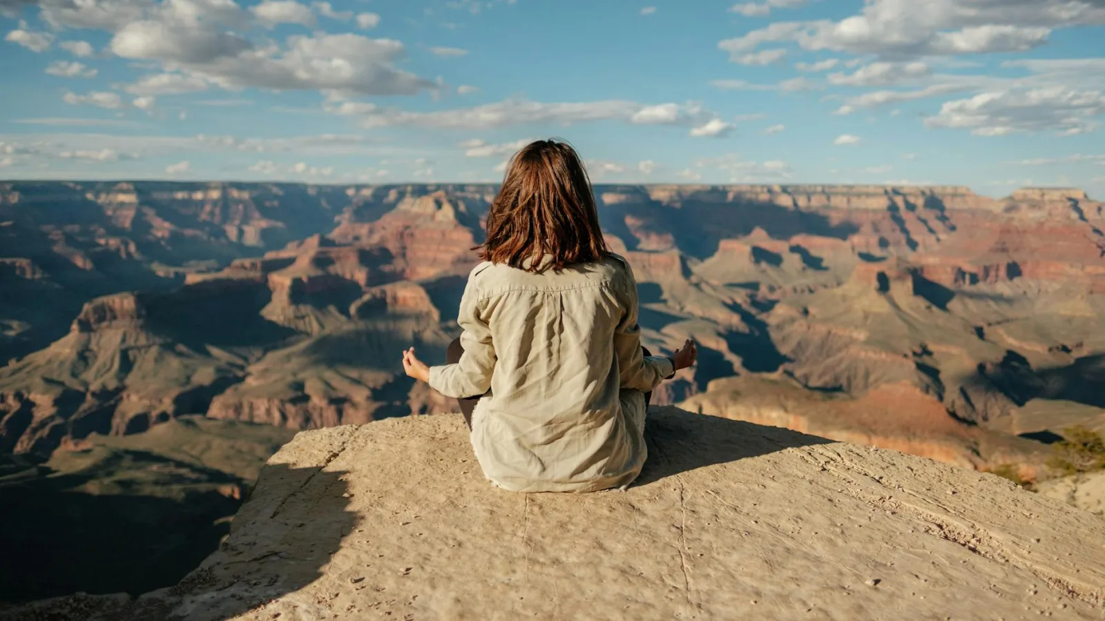 A woman practices meditation on the edge of the Grand Canyon, showcasing tranquility and nature's vastness.