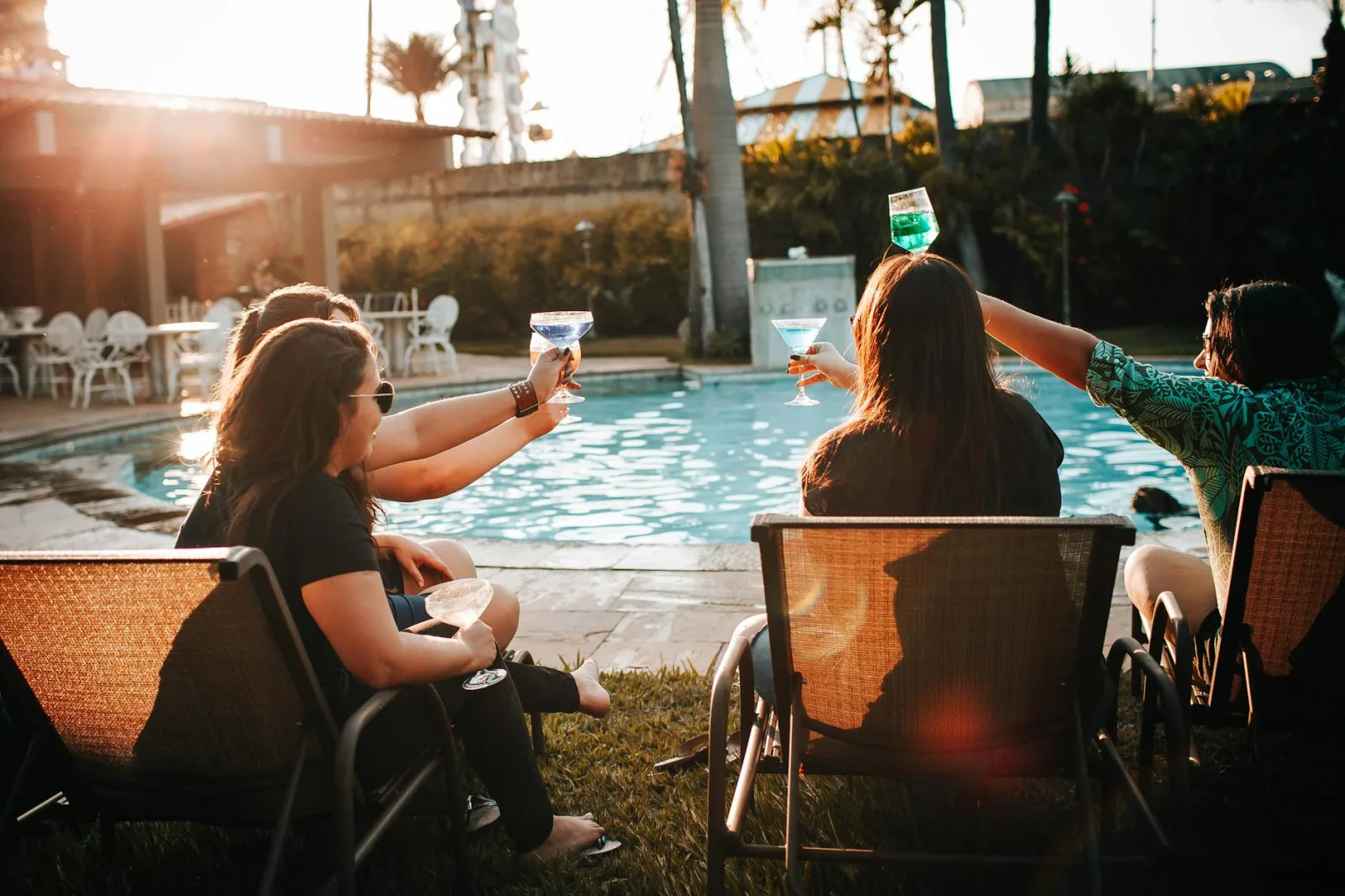 Friends relaxing with cocktails by the poolside during a sunny day, enjoying summer leisure.