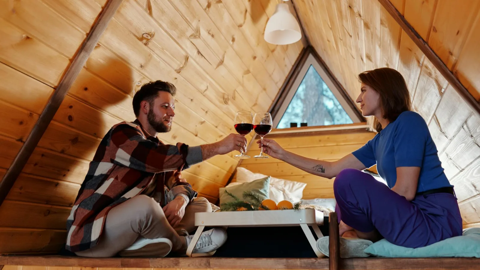 Couple enjoying a romantic evening in a cozy wooden cabin with glasses of wine.