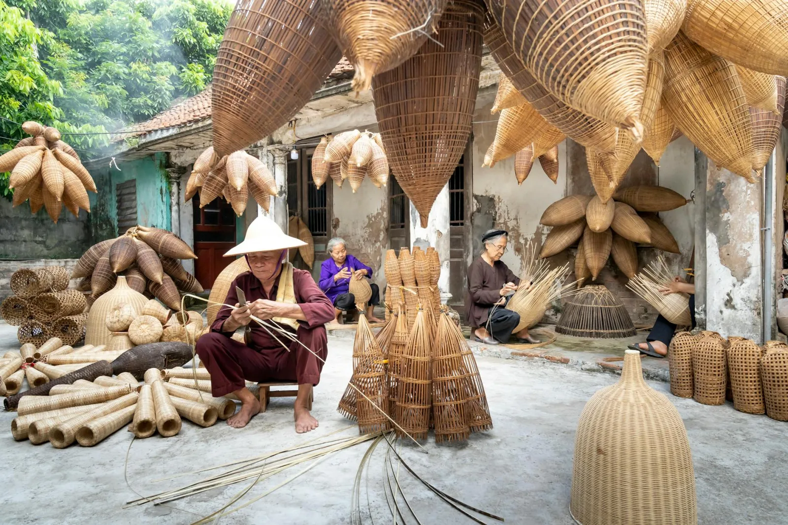 Elderly artisans crafting traditional bamboo fish traps in a sunlit courtyard.