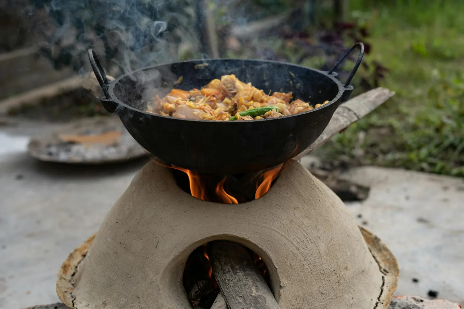 A sizzling meal cooked outdoors on a traditional clay stove with open fire, showcasing rustic culinary techniques.