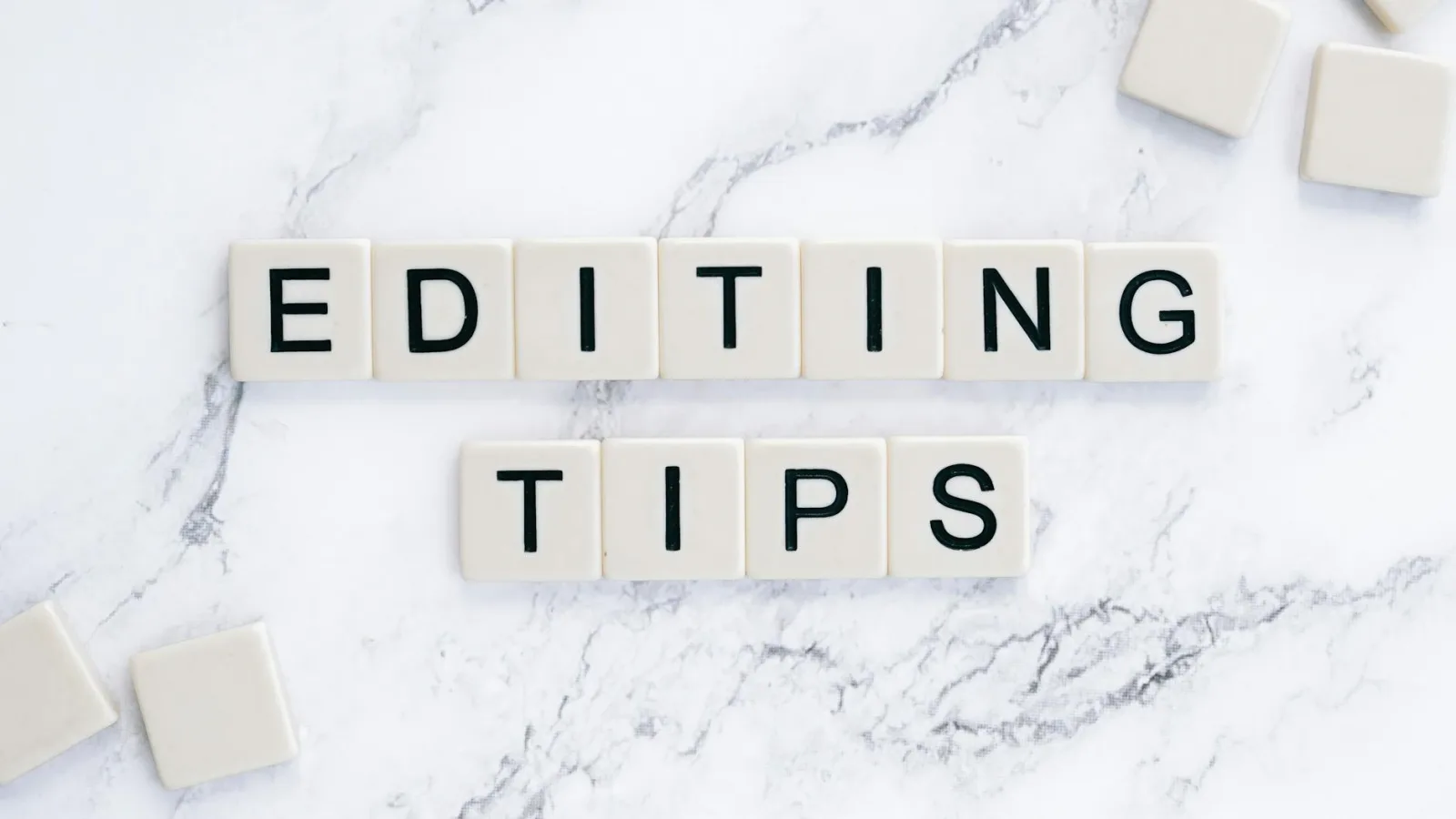 Scrabble tiles spell out 'Editing Tips' on a marble background, perfect for editorial guides.