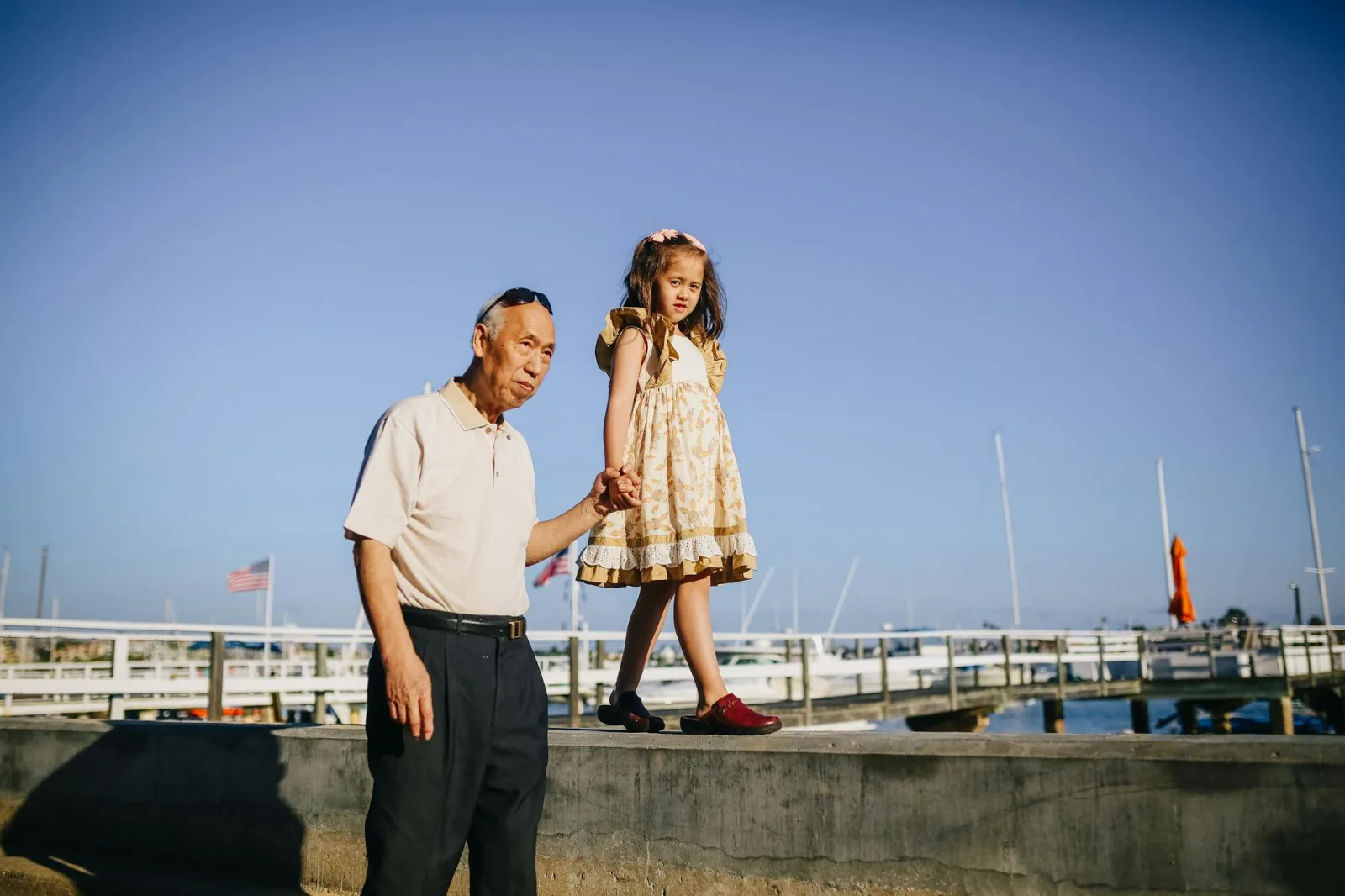 Charming moment of an elderly man and young girl holding hands and walking on a sunny pier.