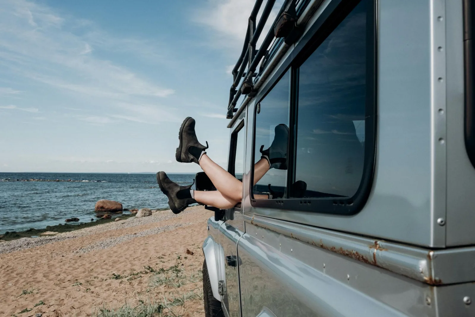 Relaxing beach scene with legs hanging out of car window, showcasing adventure and freedom.