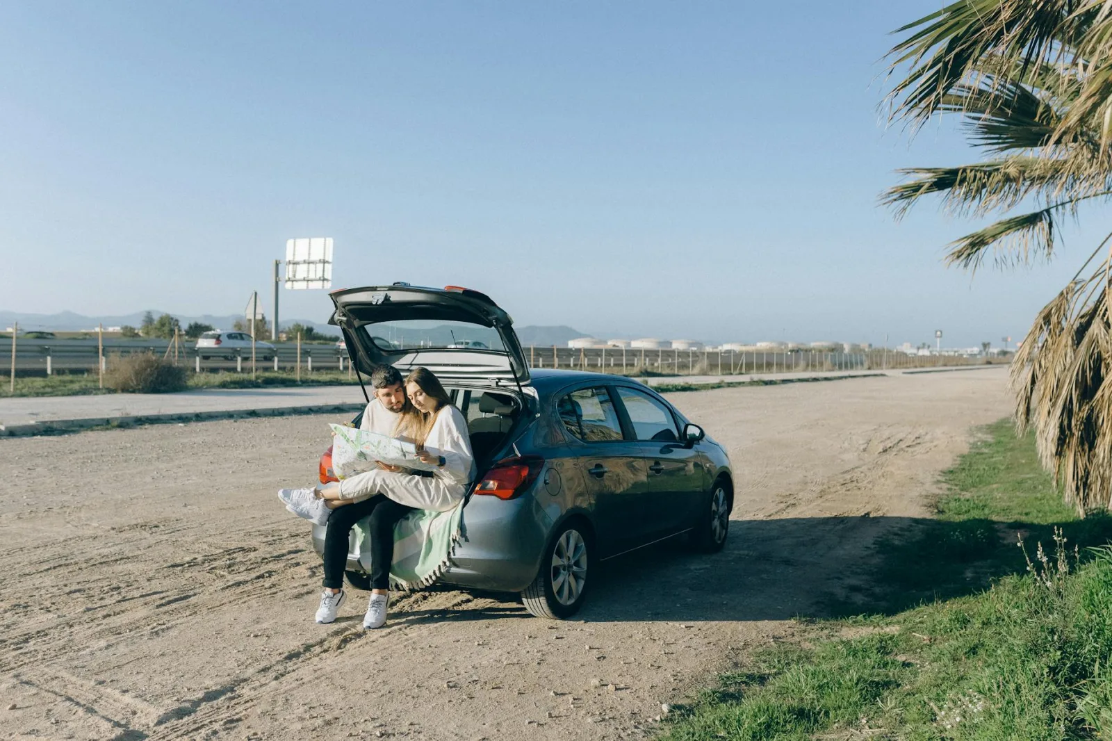 A couple sitting on car trunk exploring map during a road trip on a sunny day.