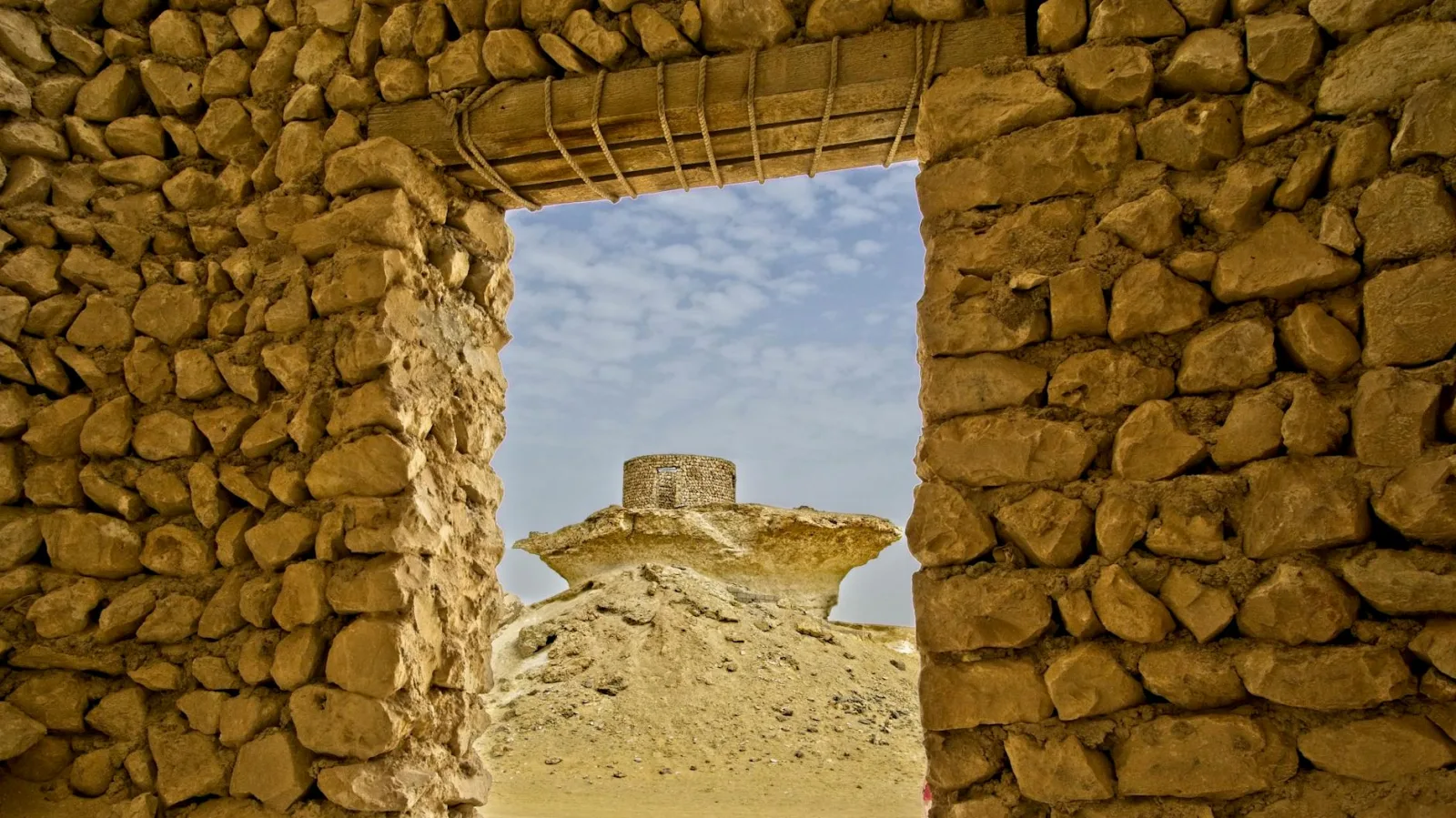 View through ancient stone ruins unveiling a desert monolith under a clear sky.