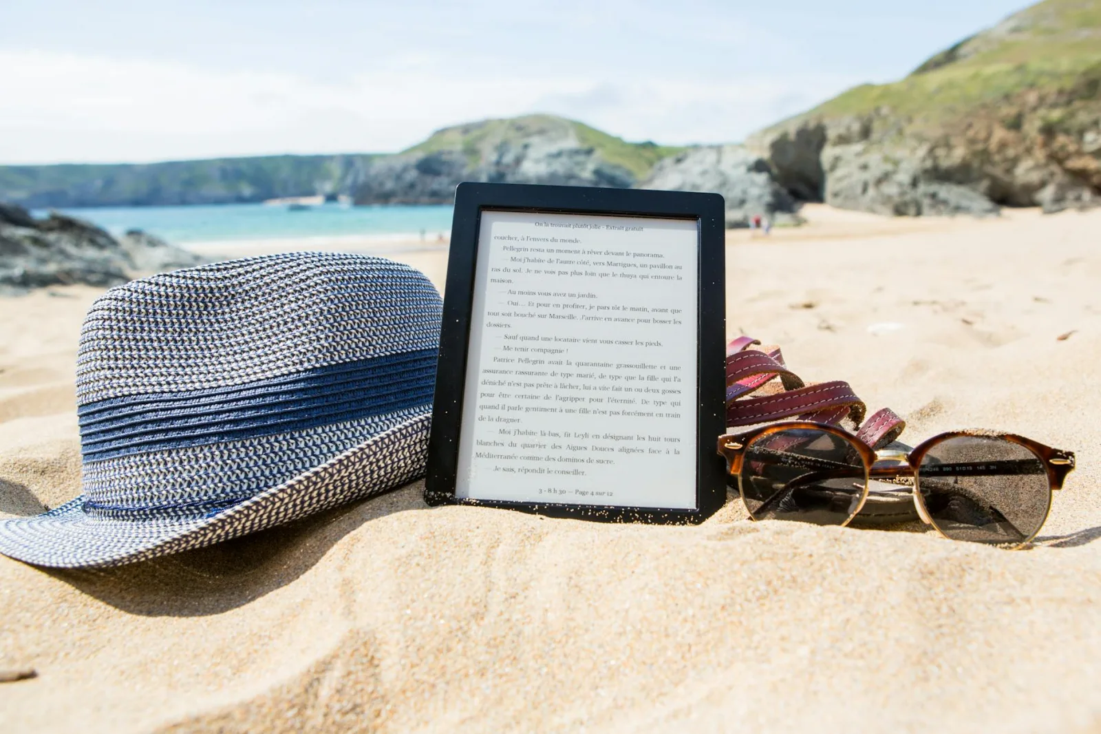 Enjoy a sunny day at Le Palais beach with an e-reader, hat, and sunglasses on the sand.