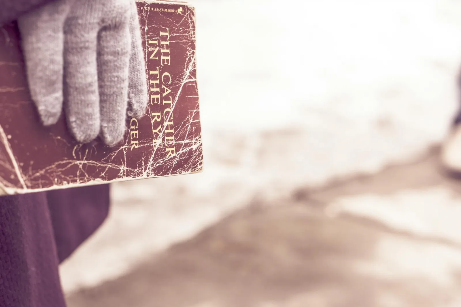 A gloved hand holds a weathered copy of The Catcher in the Rye outdoors.