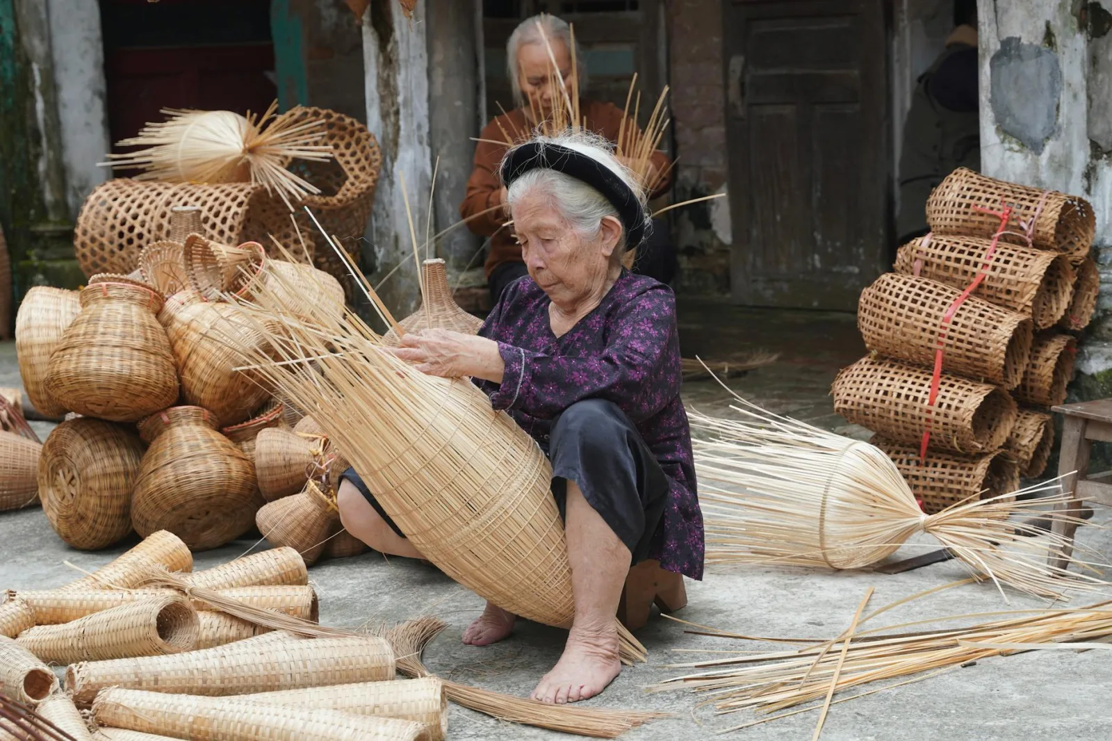 Elderly woman weaving baskets in a Vietnamese village, showcasing traditional craft.