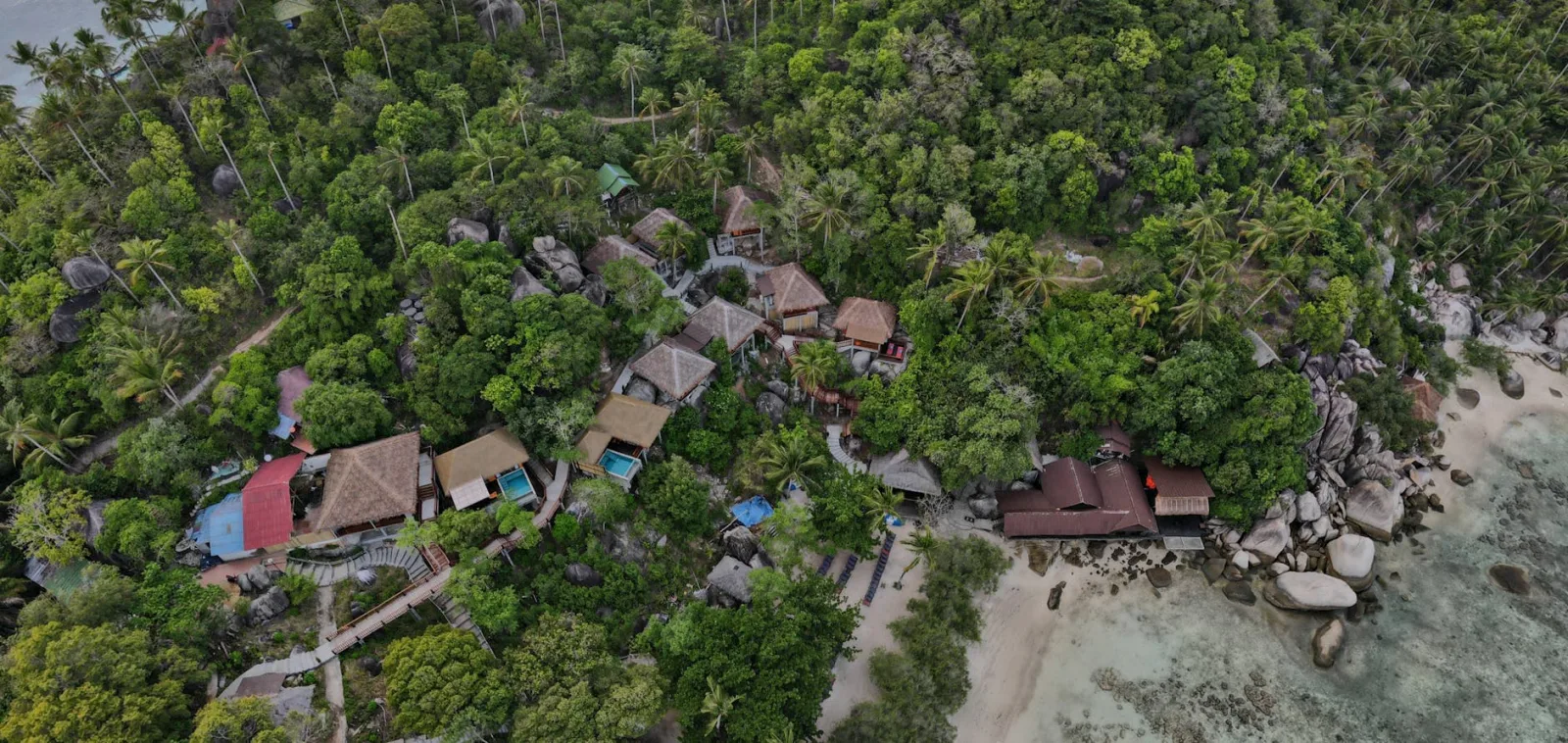 A stunning aerial view showcases a remote tropical village surrounded by lush greenery and a serene coastline.