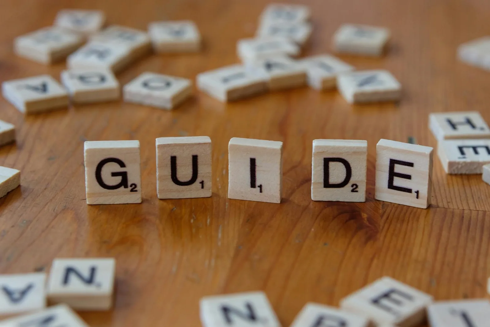 Scrabble tiles forming the word 'Guide' surrounded by scattered letters on a wooden table.