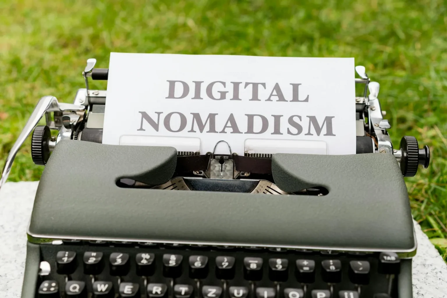 A retro typewriter outdoors with paper showing 'Digital Nomadism,' symbolizing flexible work and lifestyle.