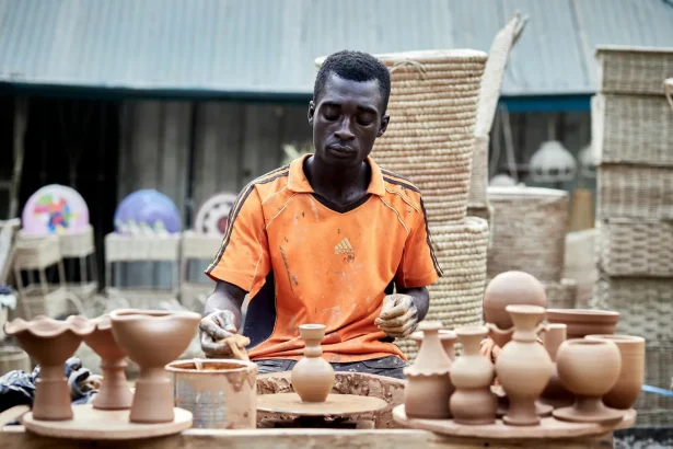 African artisan creating handmade clay pots in an outdoor market setting.