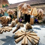 Collection of wooden fish traps hanging on ropes and placed on gray ground near weathered house and ethnic people working