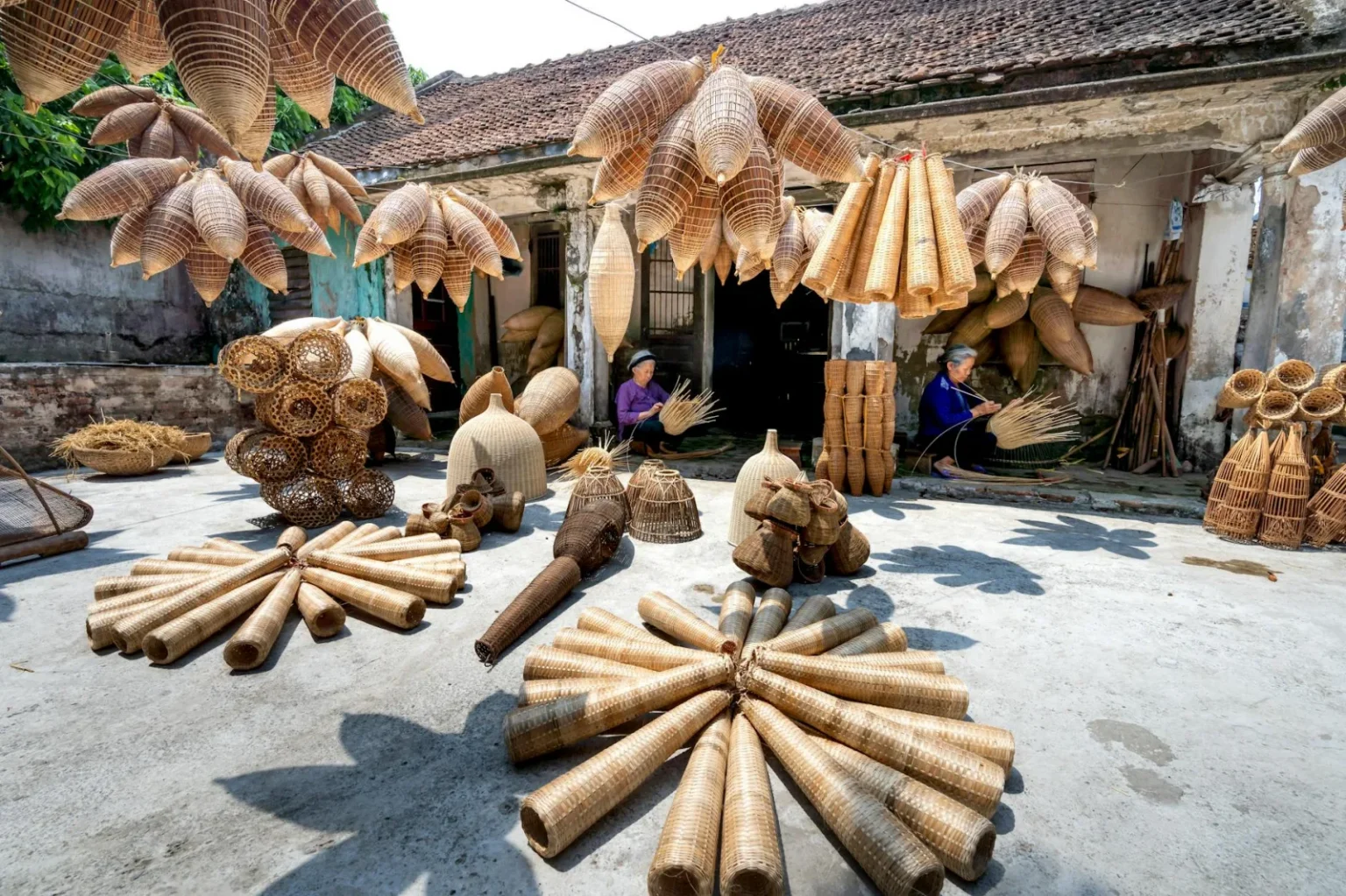 Collection of wooden fish traps hanging on ropes and placed on gray ground near weathered house and ethnic people working