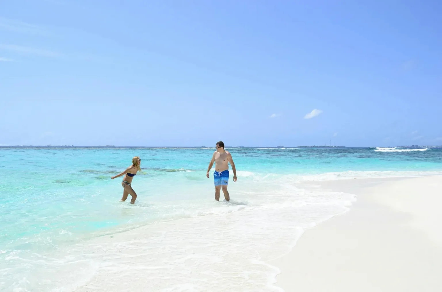 A couple enjoying a sunny day at a pristine beach with clear blue waters.
