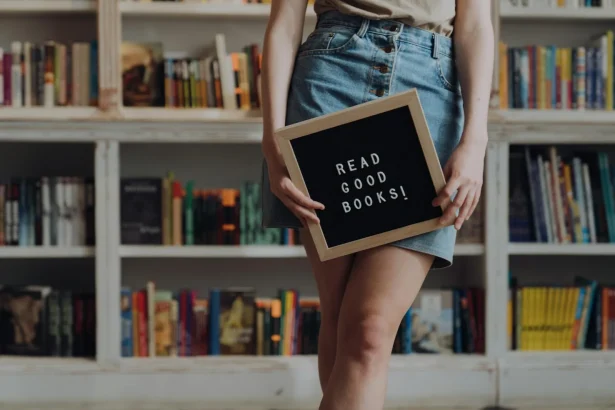 Person holding a sign with 'Read Good Books!' in a bookstore setting, encouraging reading culture.