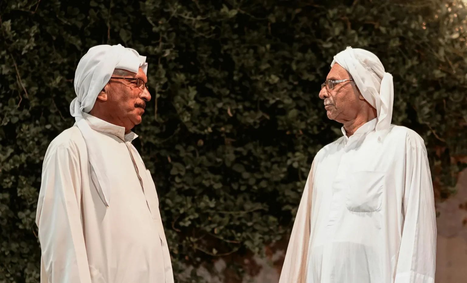 Elderly men wearing traditional Iranian attire engage in conversation outdoors.