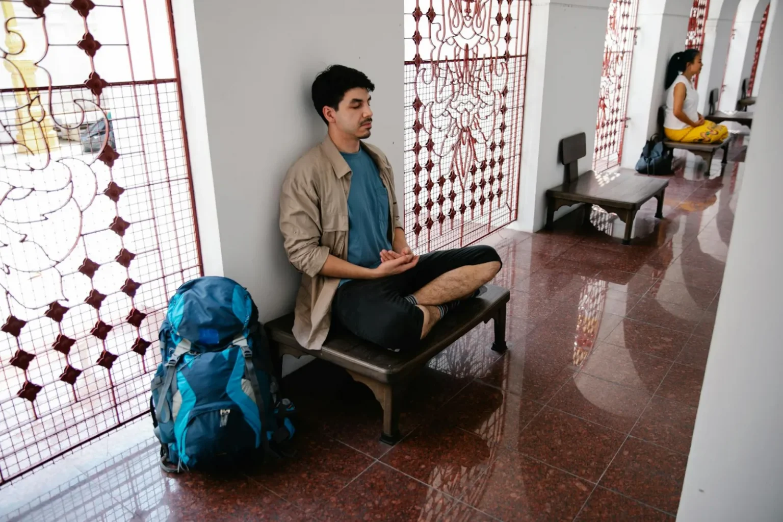A person meditating indoors, surrounded by stained glass art in a peaceful setting.