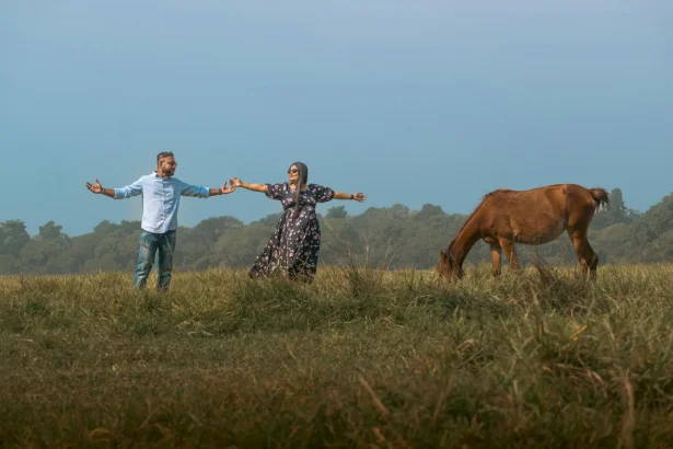 Couple holding hands in scenic Kolkata field with a horse grazing nearby.