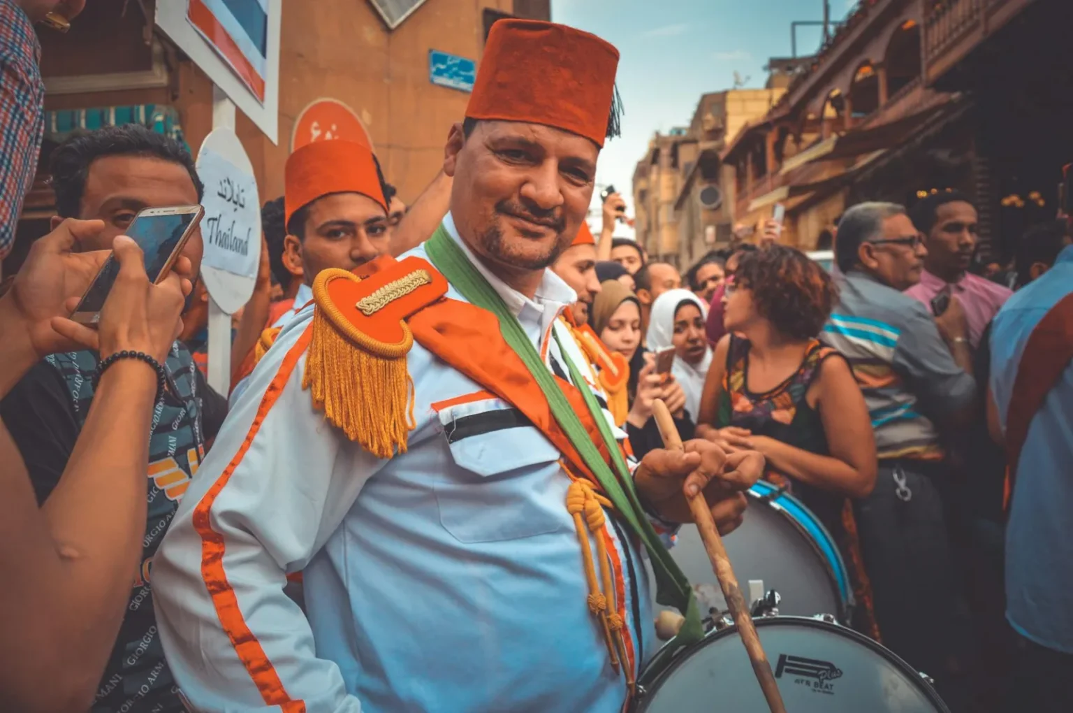 Man in traditional attire playing drums at a lively Cairo street festival.