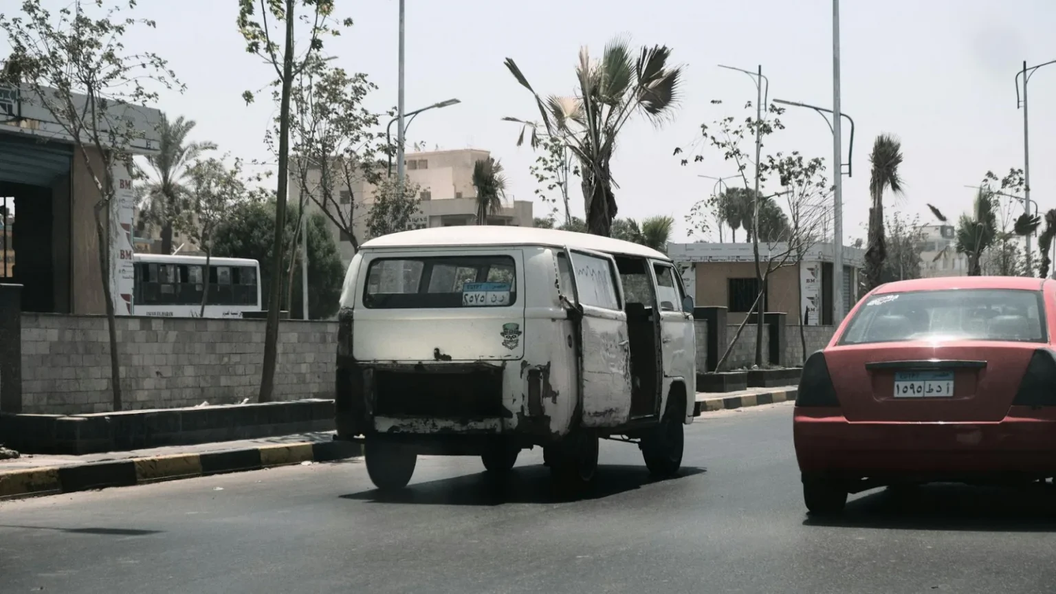 A scene of urban life featuring a vintage van and red car on a street in Cairo, Egypt.