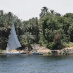 Scenic view of a traditional sailboat on the Nile River with lush greenery.