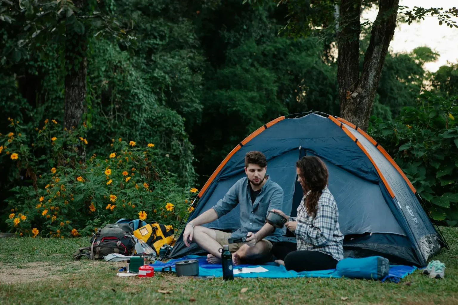 Full body of travelling young couple in casual clothes having lunch while resting near camping tent during trip in nature