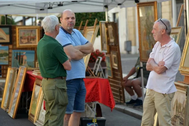 Three men conversing at an outdoor art market in Villafranca di Verona, Italy.