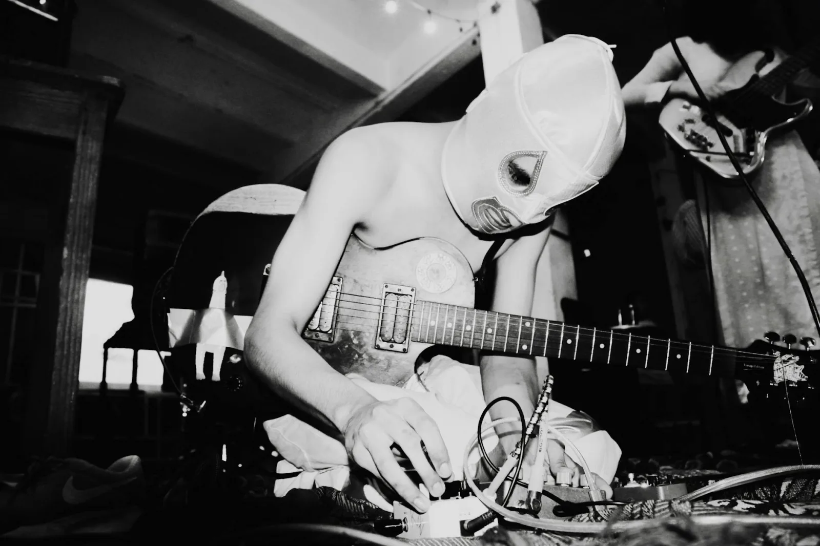 Artsy black and white photo of a masked musician adjusting guitar effects during a live performance.